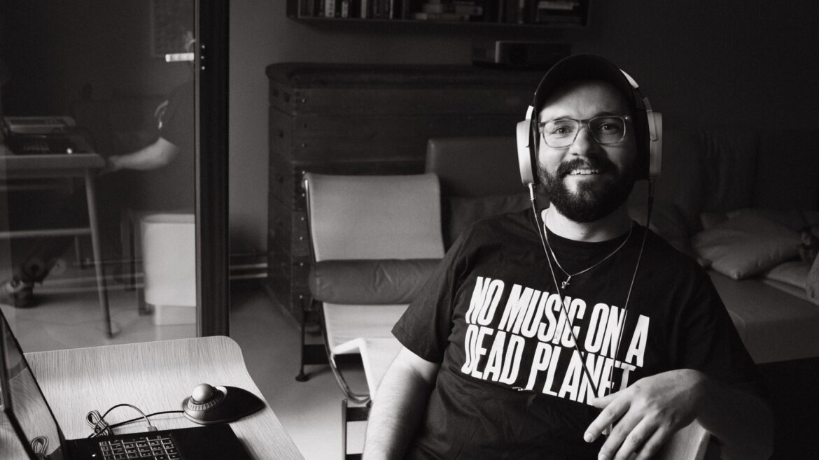 Flo Siller wearing headphones at his workstation, his shirt reads No Music on a Dead Planet