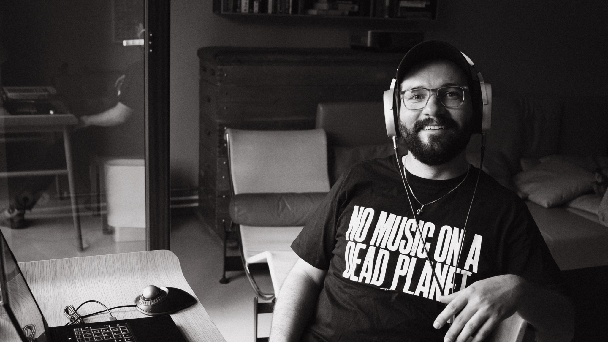 Flo Siller wearing headphones at his workstation, his shirt reads No Music on a Dead Planet