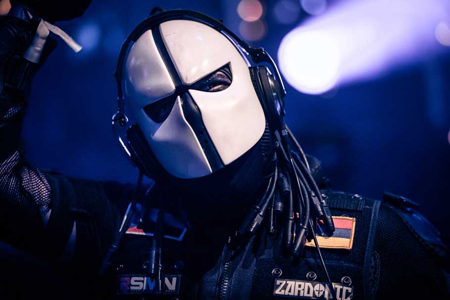 Zardonic on stage, mask head on, the Venezuelan flag on his arm